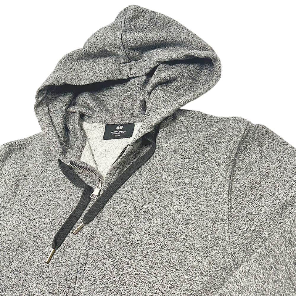 Close-up of a grey H&M zip-through hoodie with drawstrings and visible brand label on the collar.