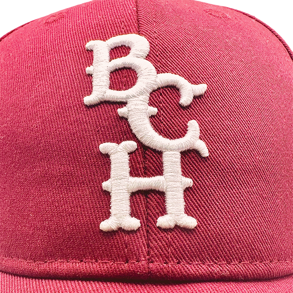 Close-up of a red Bench Baseball Cap with white embroidered "BCH" letters on the front.