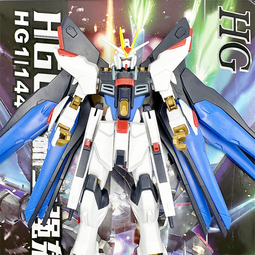 Strike Freedom Gundam figure with extended wings, displayed in front of its colorful product box.