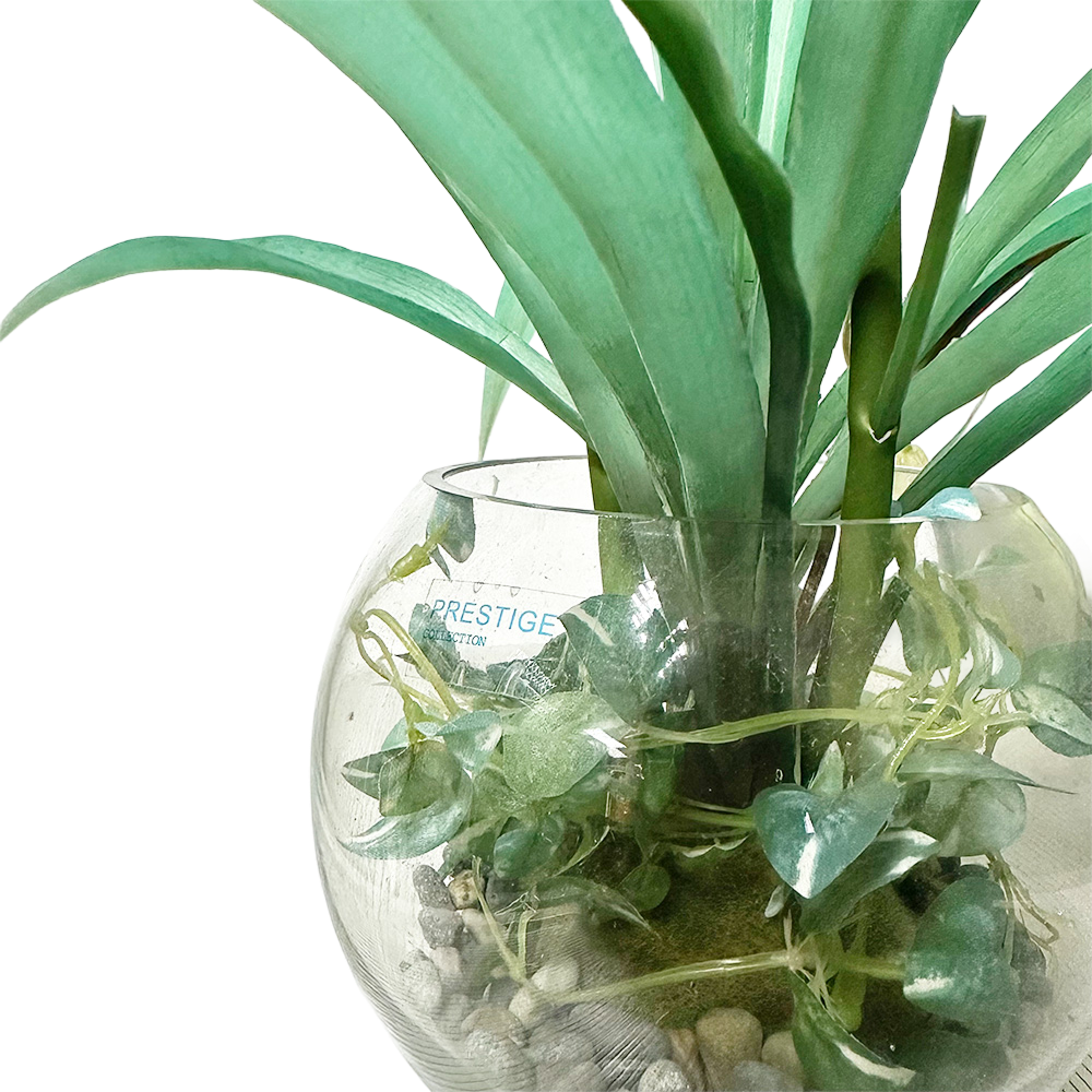 Faux topiary arrangement in a glass vase with green leaves and decorative pebbles.