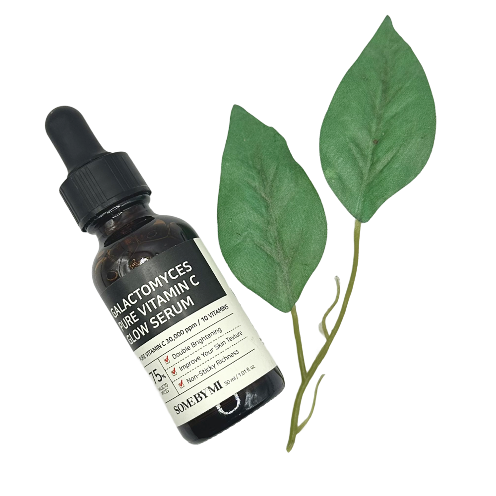 Some By Mi Vitamin C Serum bottle with dropper next to two green leaves on a white background.