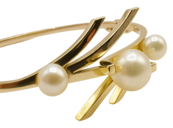 Gold bangle bracelet featuring three round white pearls and a modern, artistic design.