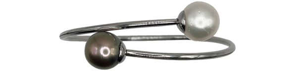 Silver bangle featuring one black pearl and one white pearl at each end, displayed on a product page.