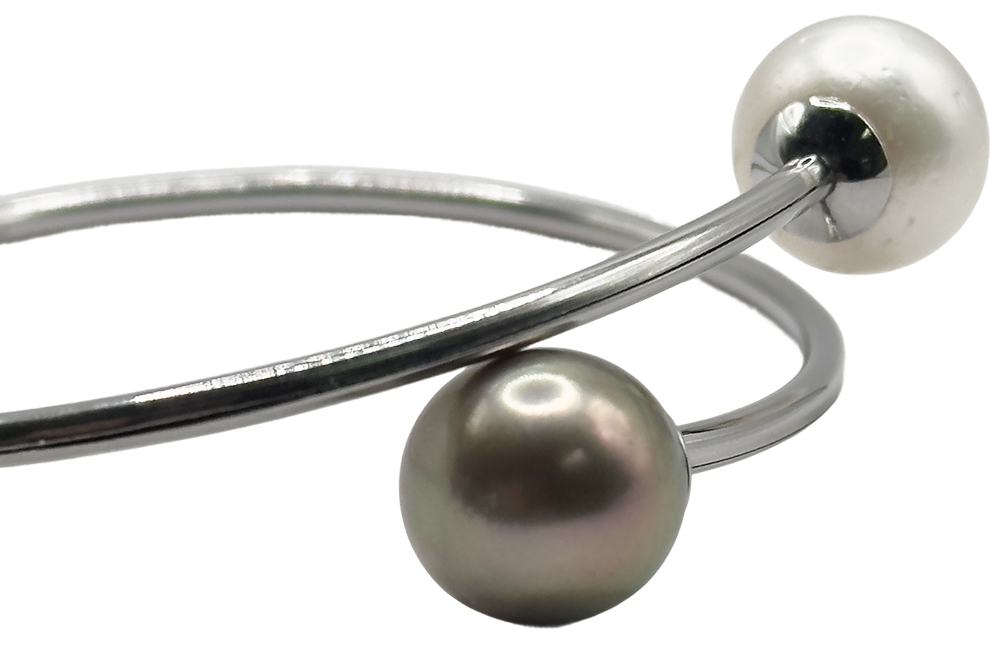 Silver bangle featuring one black pearl and one white pearl on each end, displayed against a white background.